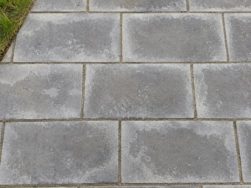 Grey rectangular concrete pavers with a cloudy whitish film that is thickest along the sand joints and thins toward the middle of each paver