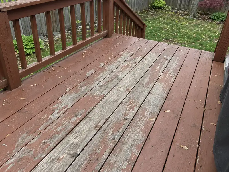 Old reddish-brown solid stain flaking off a backyard deck floor along the walking path, with bare grey wood showing through