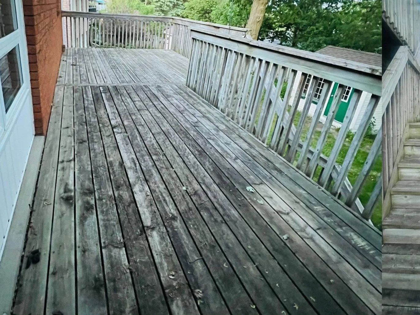 Grey, weathered wooden deck and stairs beside a brick wall