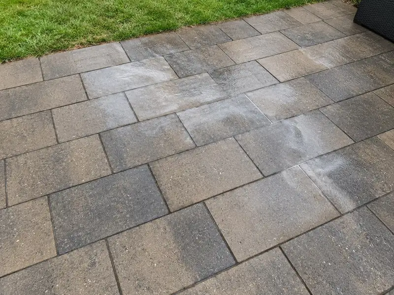 Tan and charcoal concrete patio pavers with cloudy white patches and streaks in the clear sealer, fading into evenly sealed pavers around them
